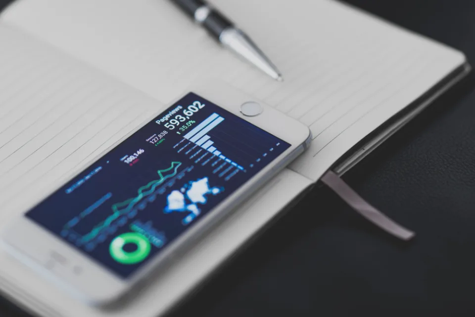 Celular sobre um caderno mostrando um painel com gráficos de origem de acessos