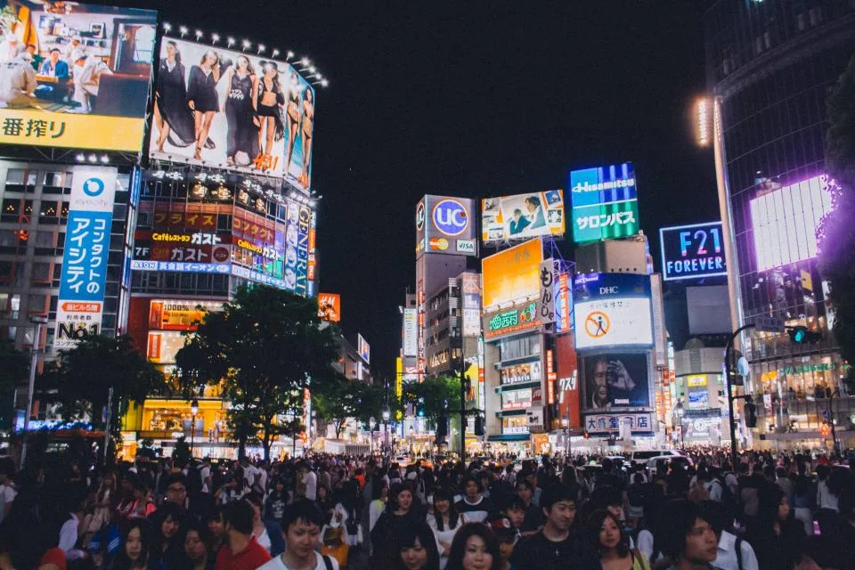 Cruzamento de Shibuya, em Tóquio, à noite, cercado por painéis publicitários luminosos e multidão atravessando