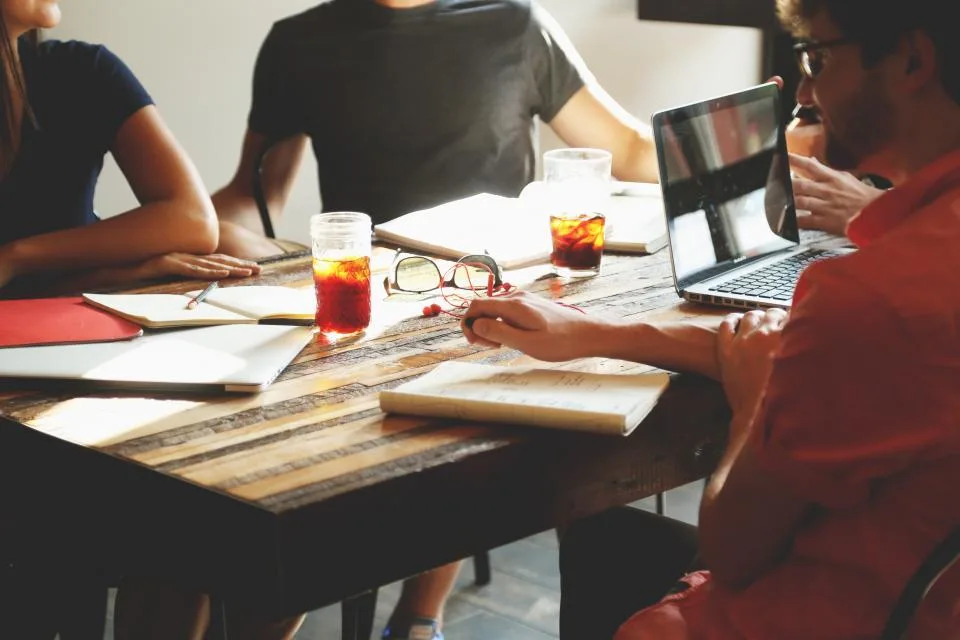 Equipe reunida em volta de uma mesa de trabalho, conversando e apontando para anotações