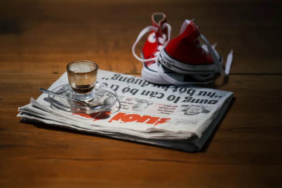 Jornal impresso aberto sobre a mesa, com xícara de café