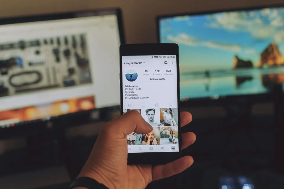 Celular exibindo um perfil de rede social, com telas de edição ao fundo