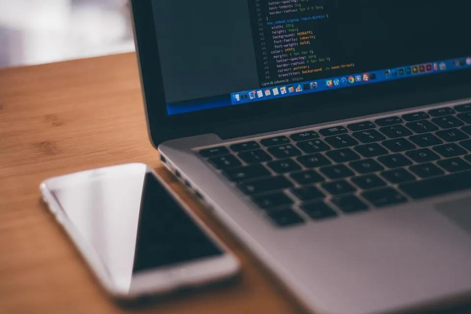 Notebook com código na tela e celular ao lado sobre a mesa