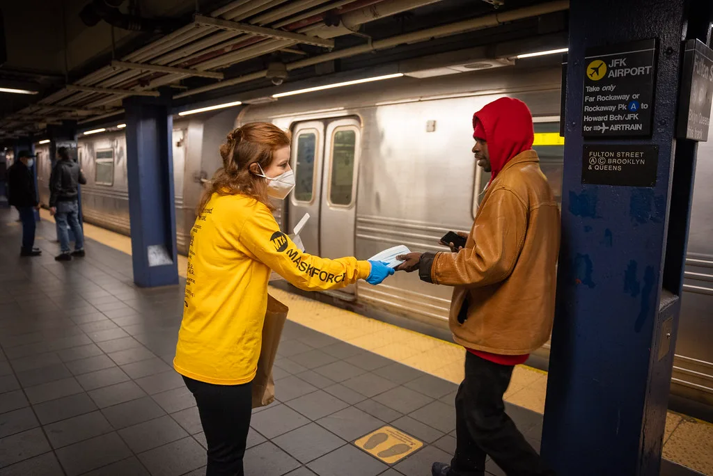 Promotora de camiseta amarela entregando material a um passageiro na plataforma do metrô