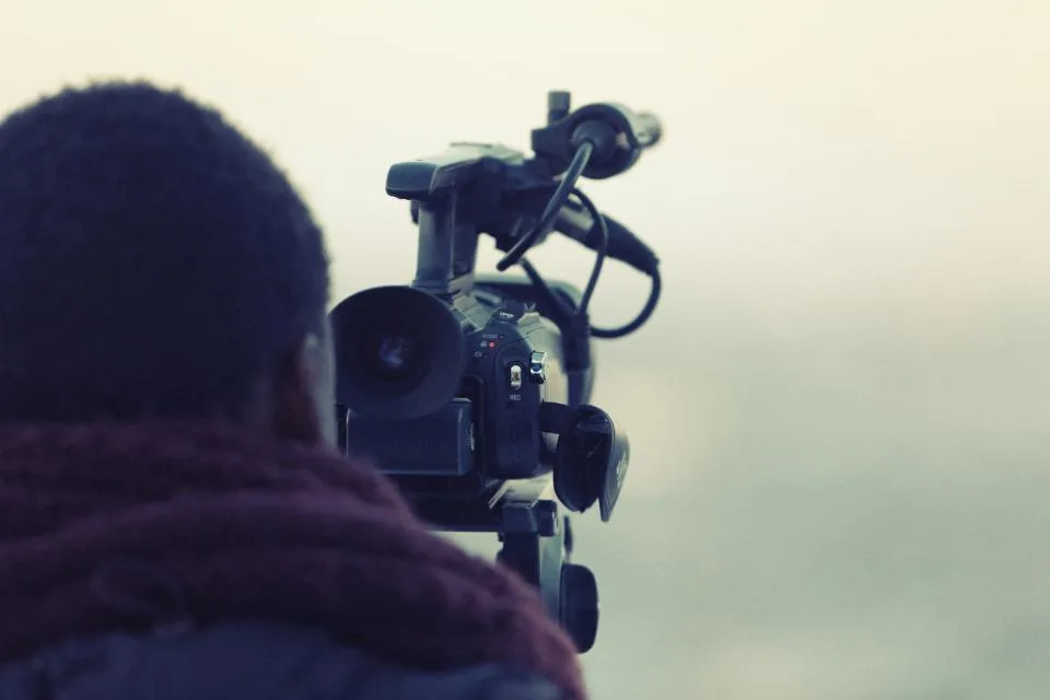 Cinegrafista de costas operando uma câmera de vídeo em um tripé
