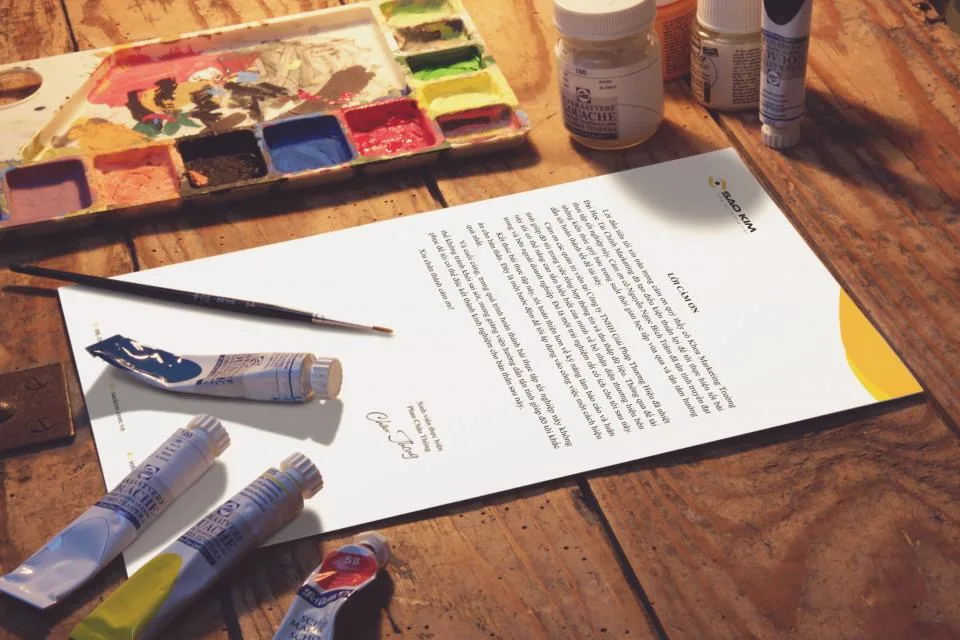 Folha timbrada de marca sobre mesa de madeira, ao lado de tintas e pincel