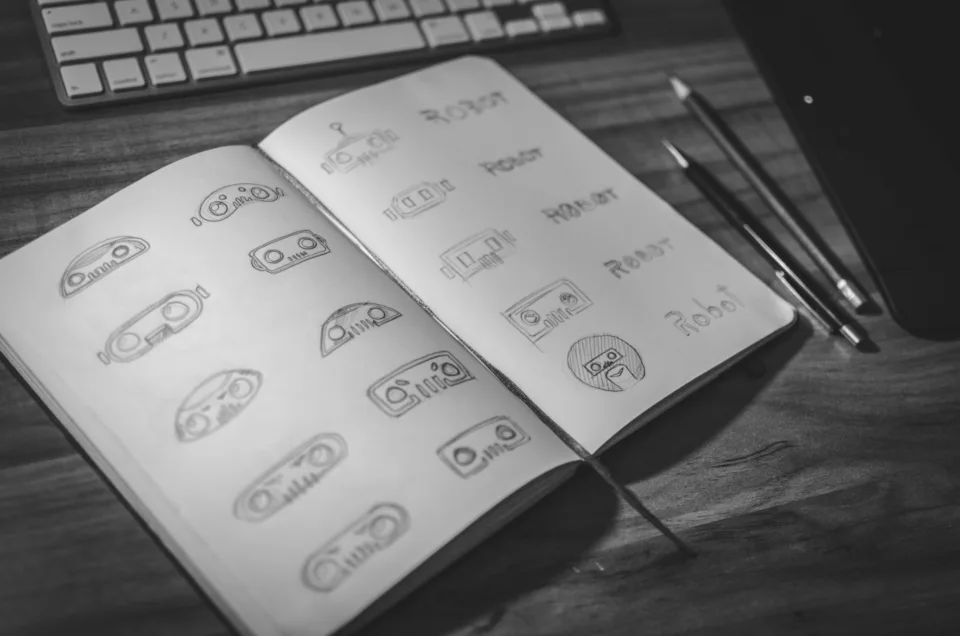 Caderno aberto com esboços de logotipo desenhados a lápis ao lado de um teclado