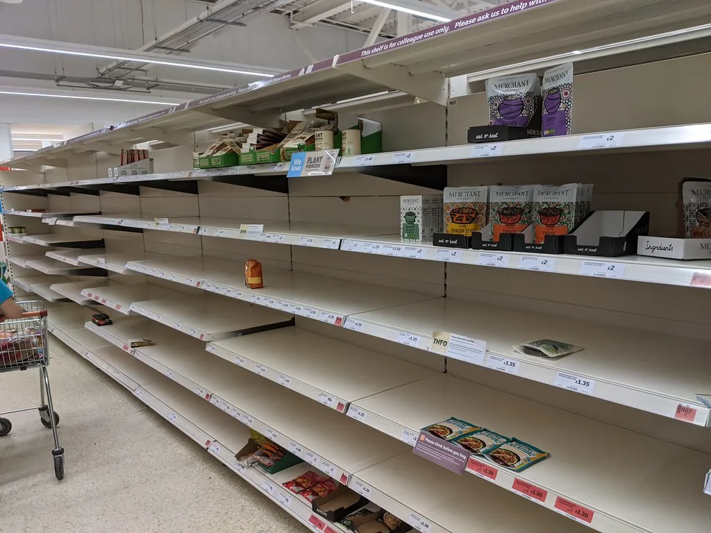 Corredor de supermercado com prateleiras quase vazias e poucos produtos restantes