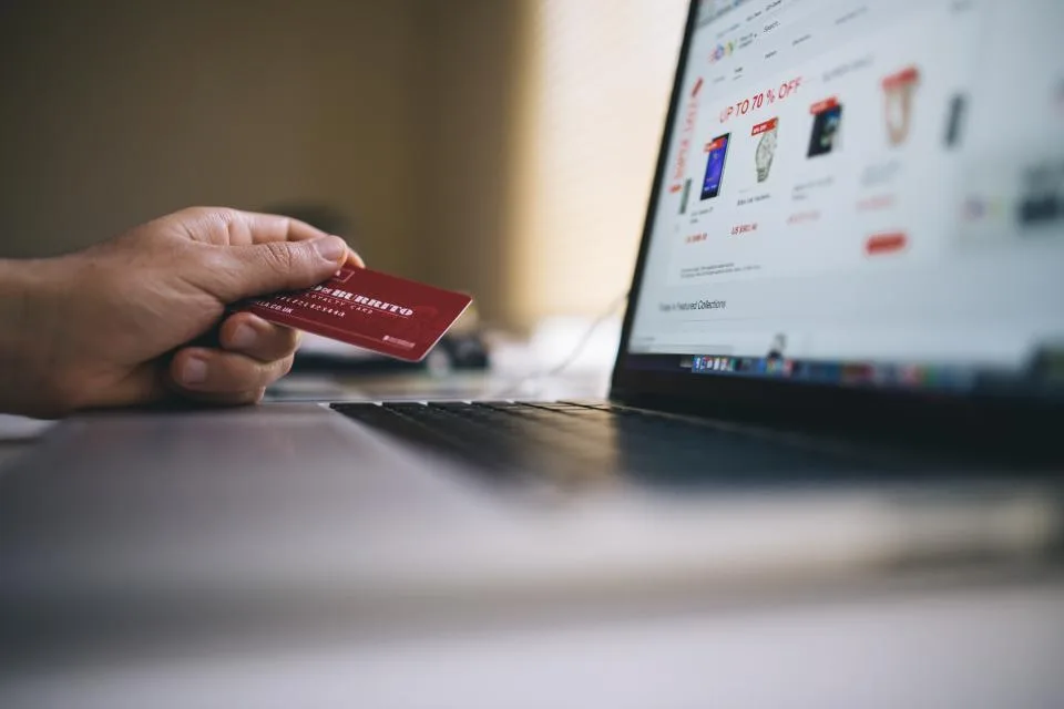 Mão segurando cartao de crédito diante de uma loja on-line aberta no notebook